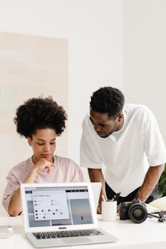 Two coworkers discussing project details over a laptop in a modern office setting.