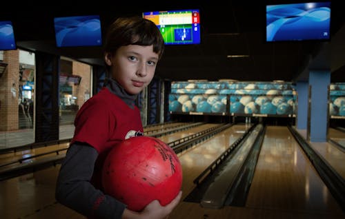 A Boy Holding a Bowling Ball While Smiling at Camera