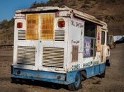 A vintage, rusty ice cream truck parked in an abandoned lot under a clear blue sky.