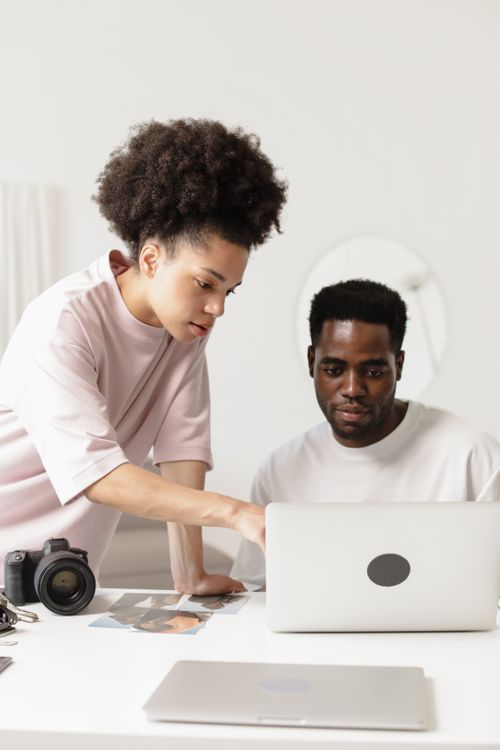 Free Two colleagues collaborating at a desk with a laptop and camera. Stock Photo