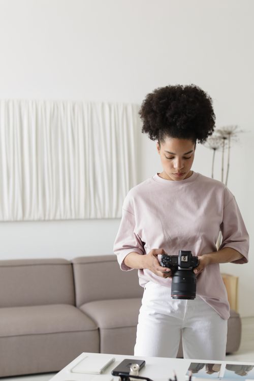 Free A young woman with afro hair reviewing photos on her DSLR indoors. Stock Photo