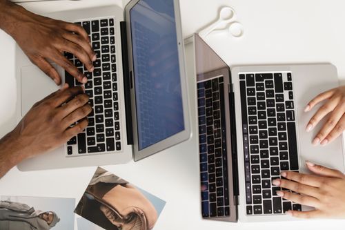 Free Two hands typing on laptops on a white desk, viewed from above, fostering teamwork. Stock Photo