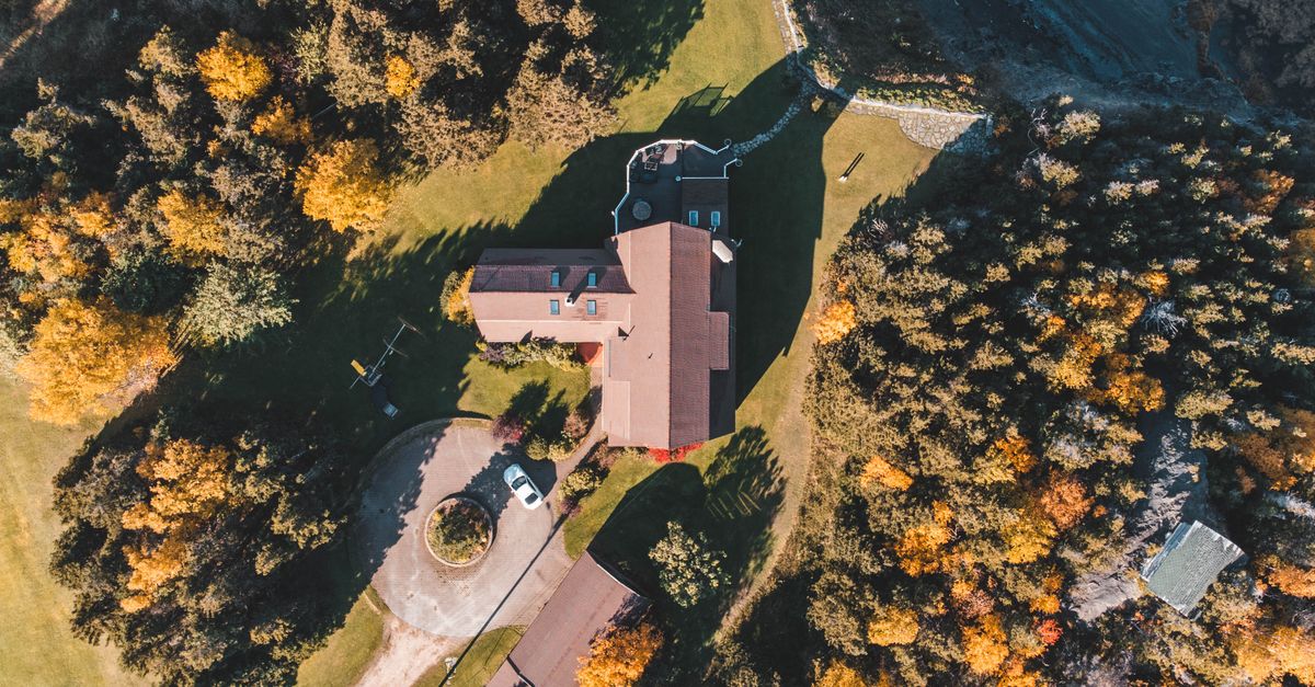 Aerial shot showcasing a countryside house surrounded by vibrant autumn trees and lush green landscapes.