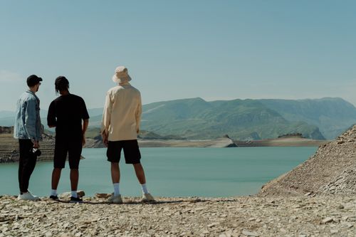 Free Three tourists overlook a breathtaking mountain reservoir under clear skies. Stock Photo