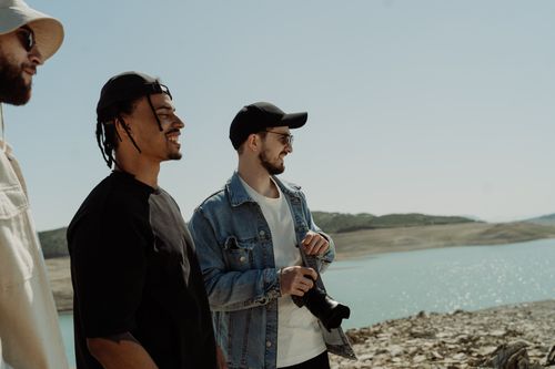 Free Three friends enjoying a sunny day by a scenic lake, capturing memories with a DSLR camera. Stock Photo