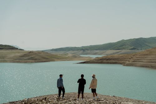 Free Three men explore a picturesque lakeside landscape with clear skies and distant mountains. Stock Photo