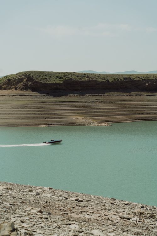 Free A motorboat speeds across a serene reservoir, framed by rugged landscapes under a clear sky. Stock Photo