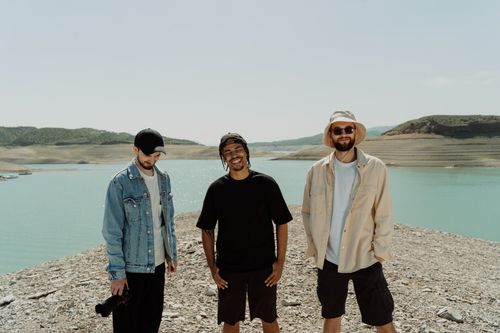 Free Three friends smiling by a picturesque reservoir on a sunny day. Stock Photo