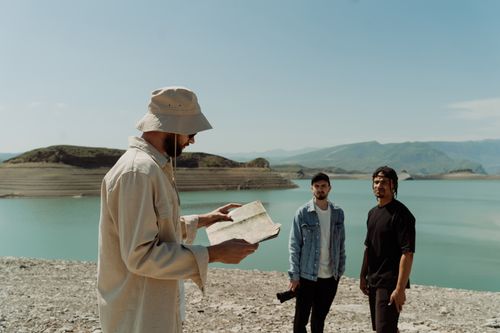 Free Three men exploring a lakeside area, strategizing their journey with a map. Stock Photo