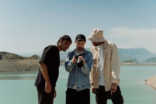 Free Three men reviewing photos on a camera by a scenic lake, embracing nature and togetherness. Stock Photo