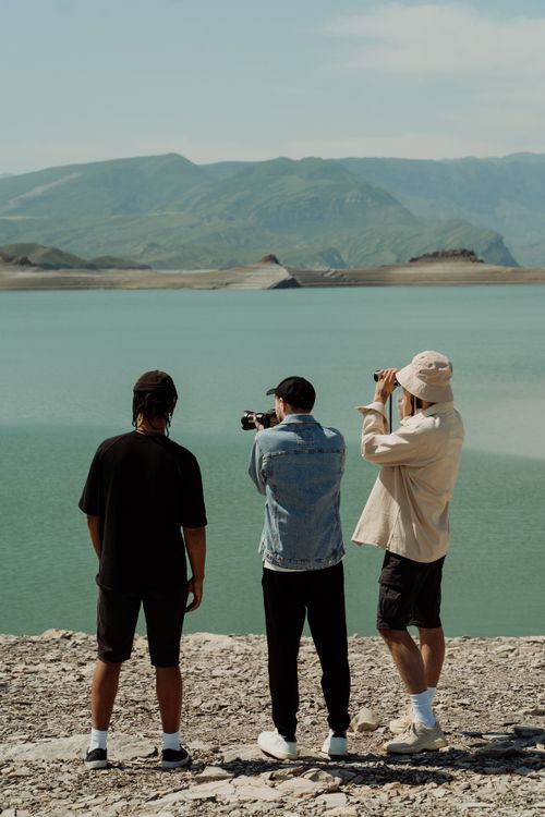Free Three friends enjoying a scenic mountain lake view, capturing memories with cameras. Stock Photo