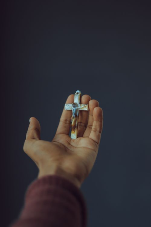 Free A contemplative image of a hand holding a crucifix against a gray background. Stock Photo