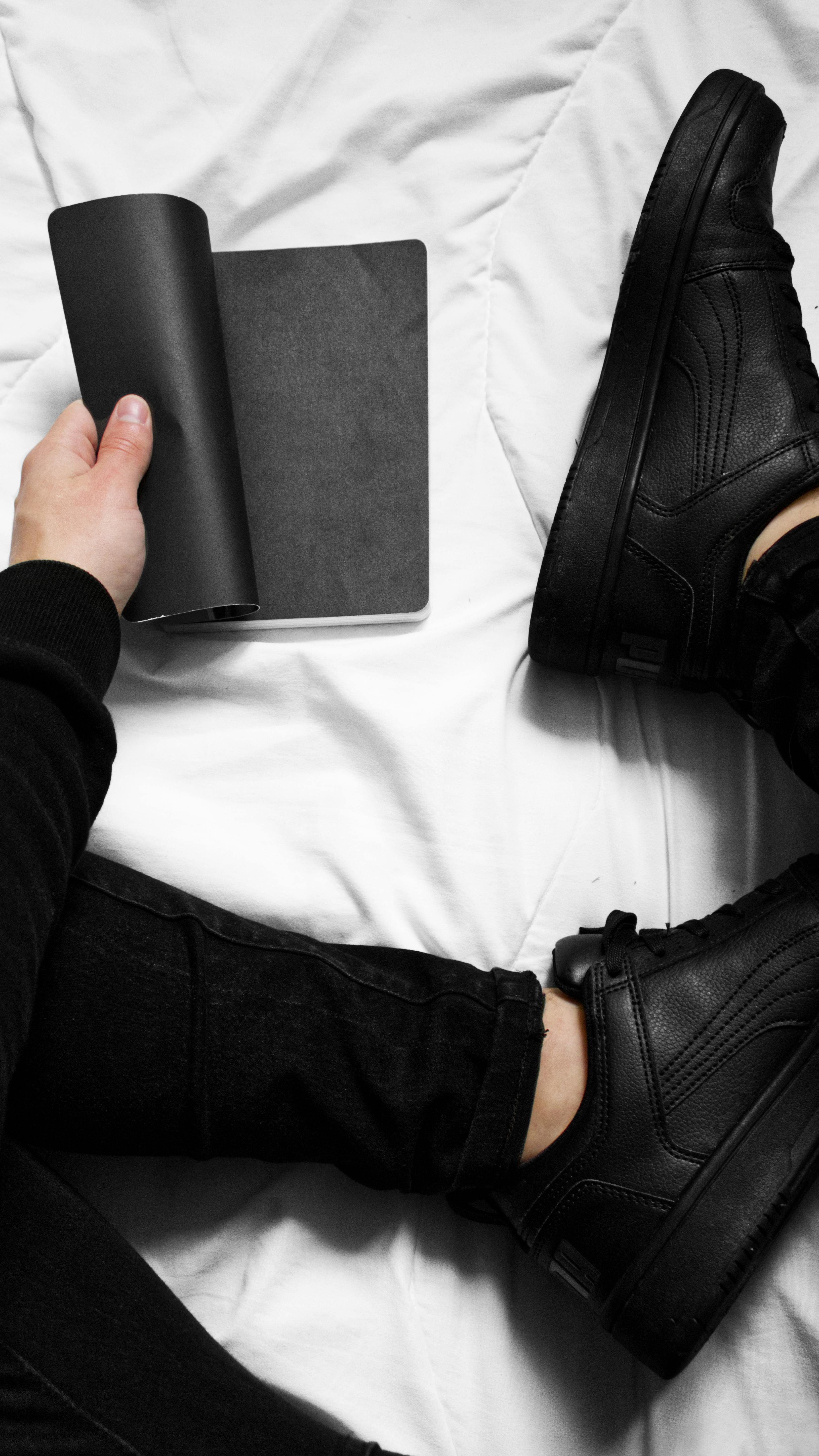 a person holding black notebook on the bed