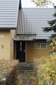 Front view of a yellow wooden house entrance in Tallinn with autumn foliage.