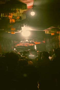 A crowded alleyway at night with people surrounded by dim, moody lighting, enhancing a mysterious atmosphere.