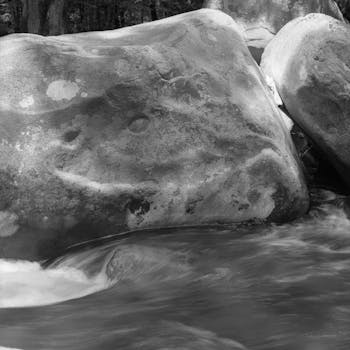 Black and white image of large rocks by a flowing stream, creating a serene winter scene.