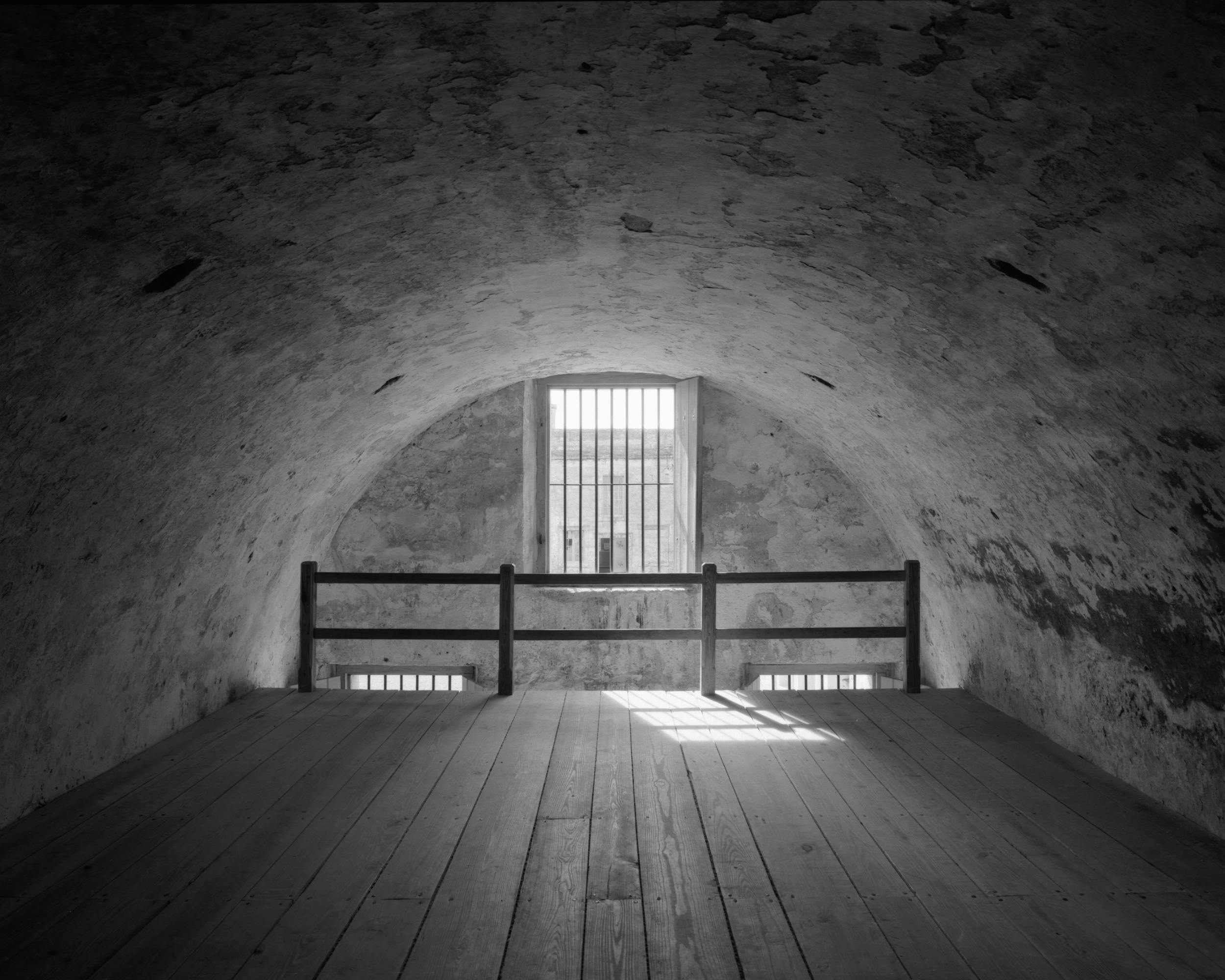 A black and white photo of an empty arched attic room with a window, St. Augustine, FL.