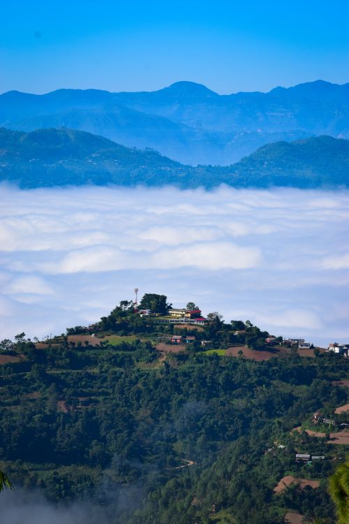 Free A breathtaking aerial view of a mountain village surrounded by lush greenery and cloud-covered valleys. Stock Photo