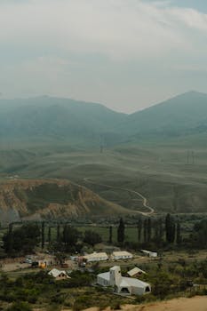 A tranquil rural scene with mountains and lush greenery under a clear sky.