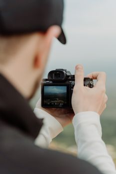 Back view of a photographer focusing a camera on a picturesque landscape outdoors.
