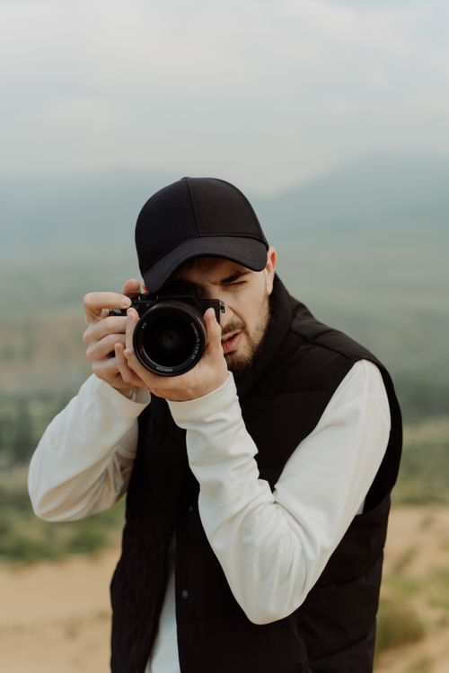 Free Photographer with camera taking a photo in a scenic outdoor setting, wearing a casual outfit. Stock Photo