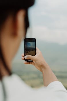 A person taking a photo with a smartphone outdoors, capturing a scenic view.