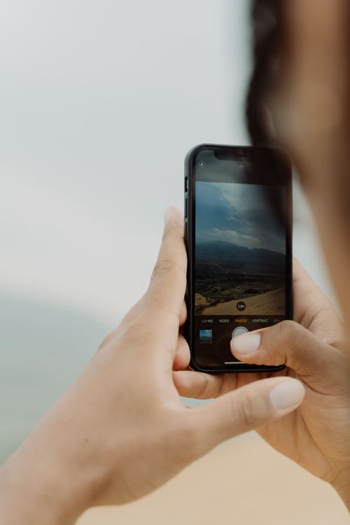 Free Close-up image of a person using a smartphone to capture a scenic outdoor view. Stock Photo