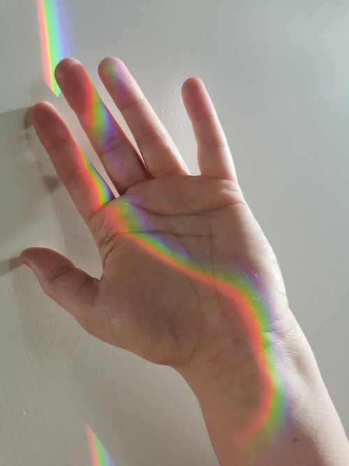 Free Close-up of a hand with a vibrant rainbow reflection on a white wall indoors. Stock Photo