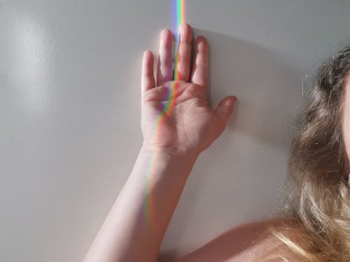 A Person's Hand With Rainbow Light Reflection Leaning on the Wall 