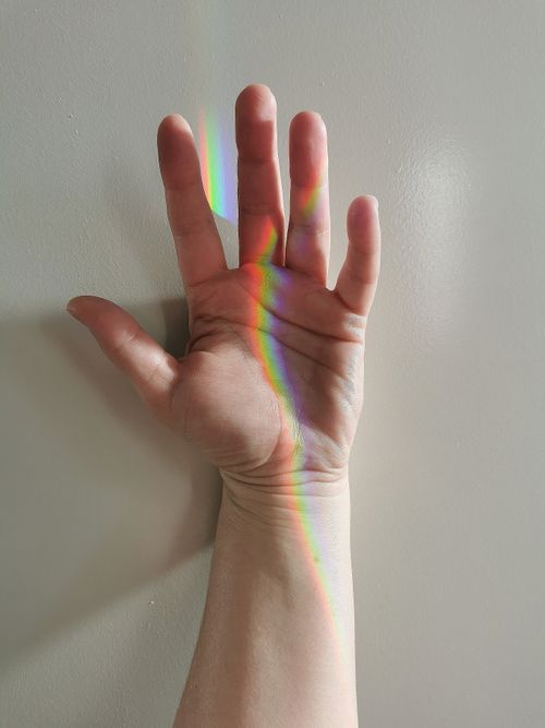 Free Hand against a white wall with a rainbow light reflection creating a colorful pattern. Stock Photo