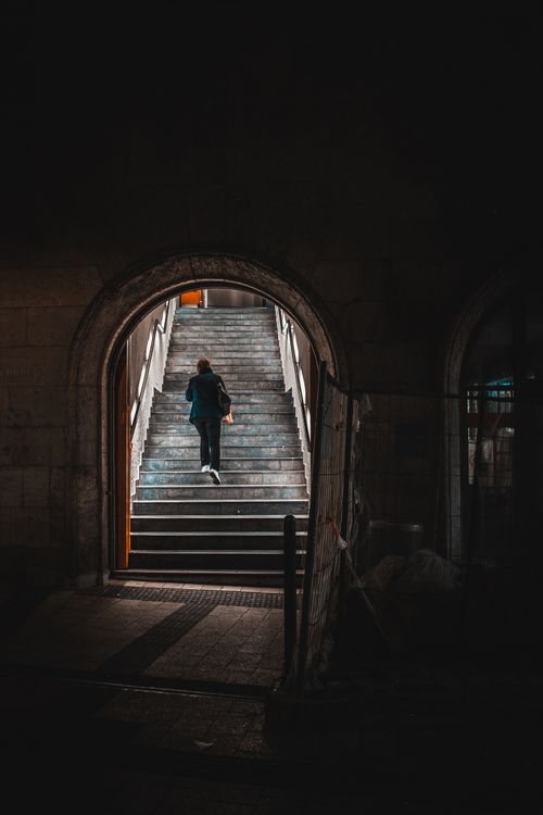 Free Silhouette of a person climbing stairs through an archway at night, casting dramatic shadows. Stock Photo