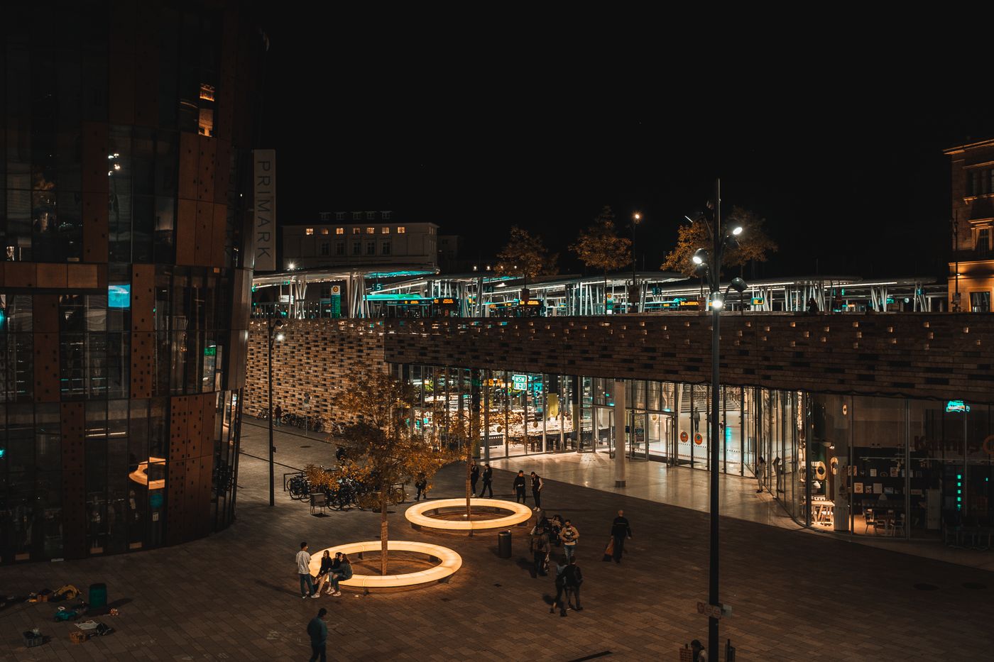 Beleuchtete Platzszene bei Nacht mit leuchtenden Ringen und einer Brücke im Hintergrund