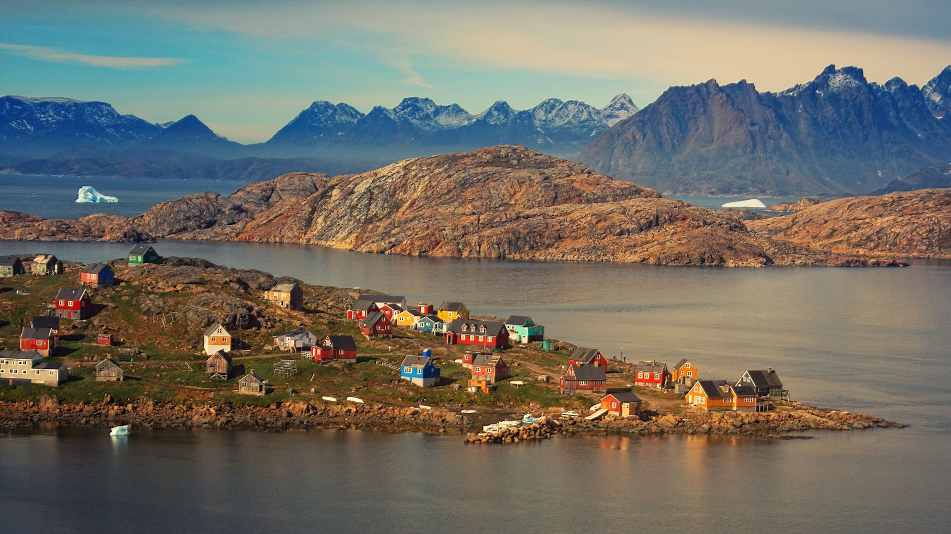 Aerial view of Kulusuk village, colorful houses against rugged mountains in Greenland.
