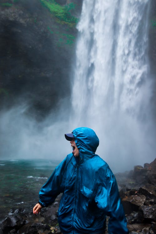 A Person in Blue Raincoat Standing Near a Beautiful Waterfalls