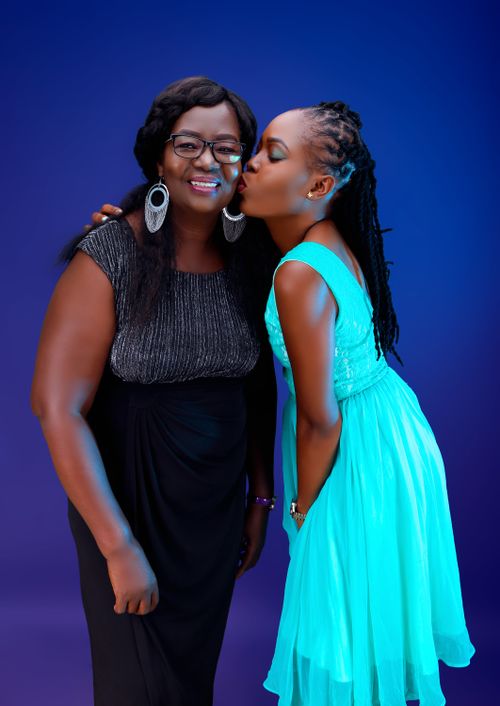Free A heartwarming portrait of a mother and daughter sharing a kiss against a vibrant blue backdrop. Stock Photo