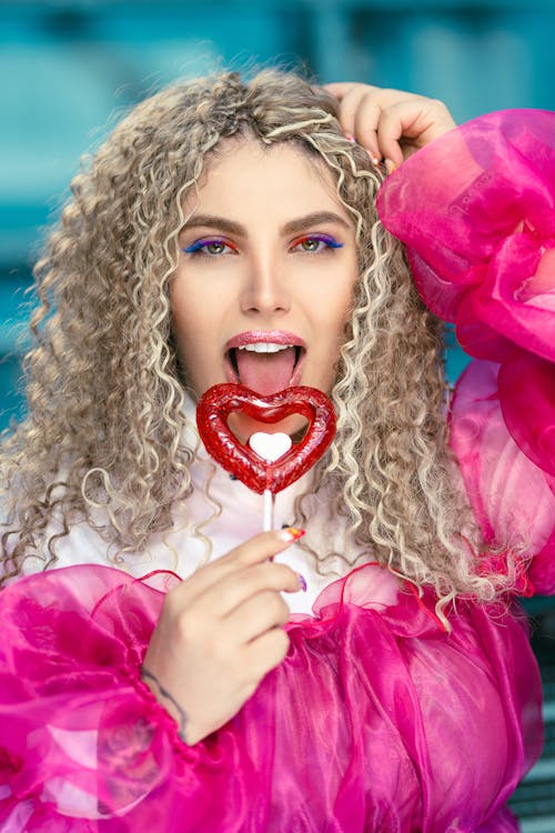 Free Woman in Pink Long Sleeve Shirt Holding Red Heart Shaped Lollipop Stock Photo