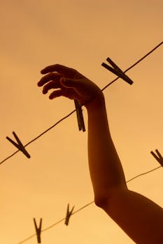 A dramatic view of a silhouetted hand reaching for clothespins against an orange sunset sky.