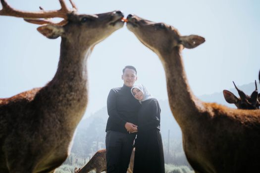 Couple embracing tenderly surrounded by deer in an outdoor setting, capturing love and nature. - Fotografer Sidoarjo
