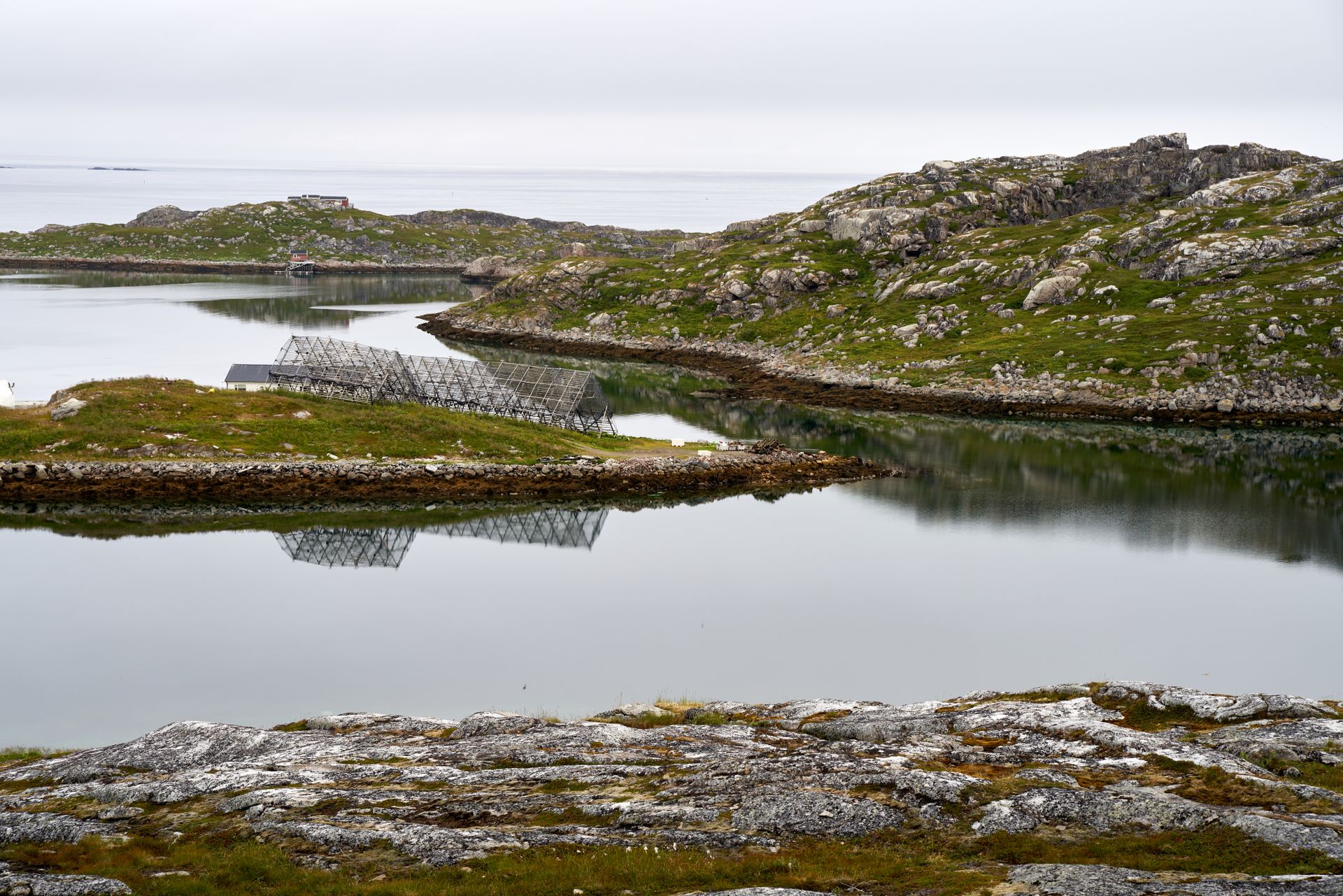 Tranquil lake surrounded by rocks and grass with solar panel reflections.