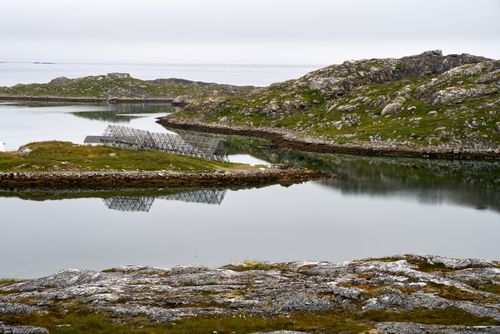 Free Tranquil lake surrounded by rocks and grass with solar panel reflections. Stock Photo