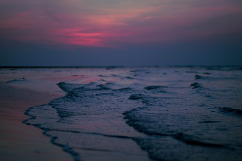 Free A tranquil ocean scene with gentle waves and a vibrant pink sunset sky. Stock Photo