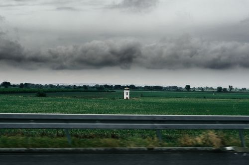 Free Moody sky over a green field with highway in foreground, showcasing nature's drama. Stock Photo