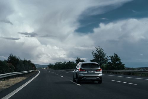 Free A silver SUV travels on a highway surrounded by lush greenery and dramatic clouds. Stock Photo