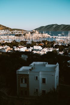Scenic aerial view of a coastal city with a marina and surrounding hills under a clear sky.