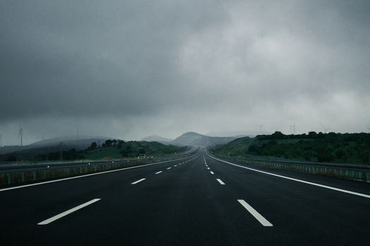 A tranquil empty highway stretches into the distance under moody overcast skies.