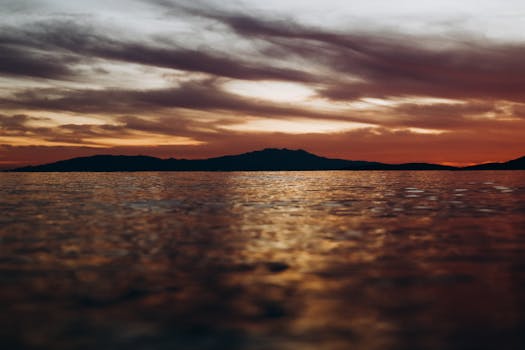 Beautiful sunset with calming ocean waves and silhouetted mountains on the horizon.