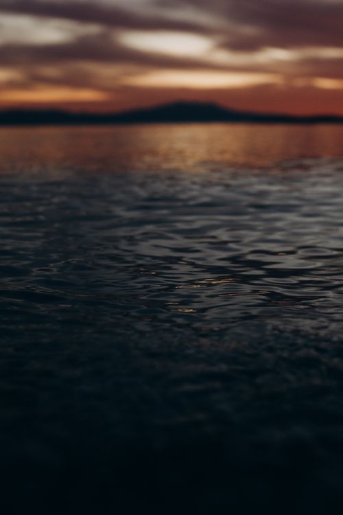 Free A tranquil ocean scene at twilight with a mountain silhouette and vibrant sky. Stock Photo