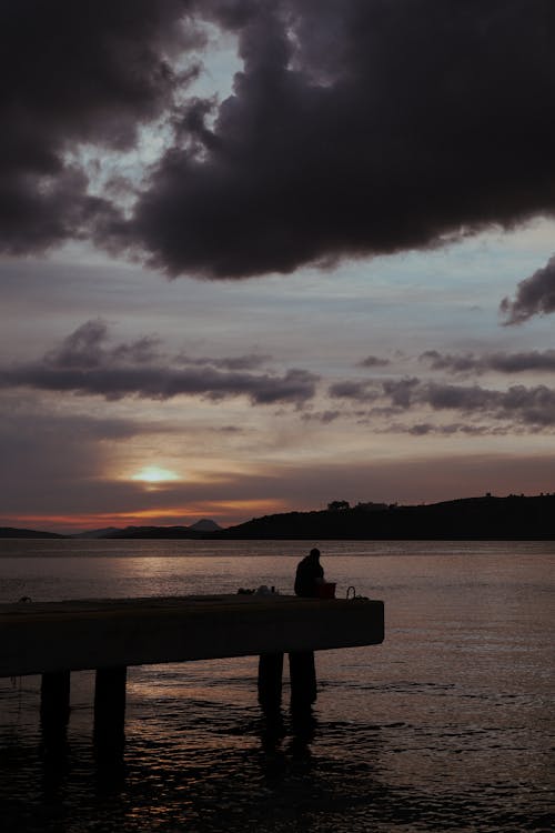 Free Silhouette of a Person sitting on a Dock  Stock Photo