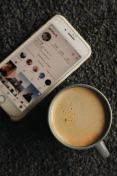 Top view of a cappuccino with a smartphone displaying Instagram on a carpet.