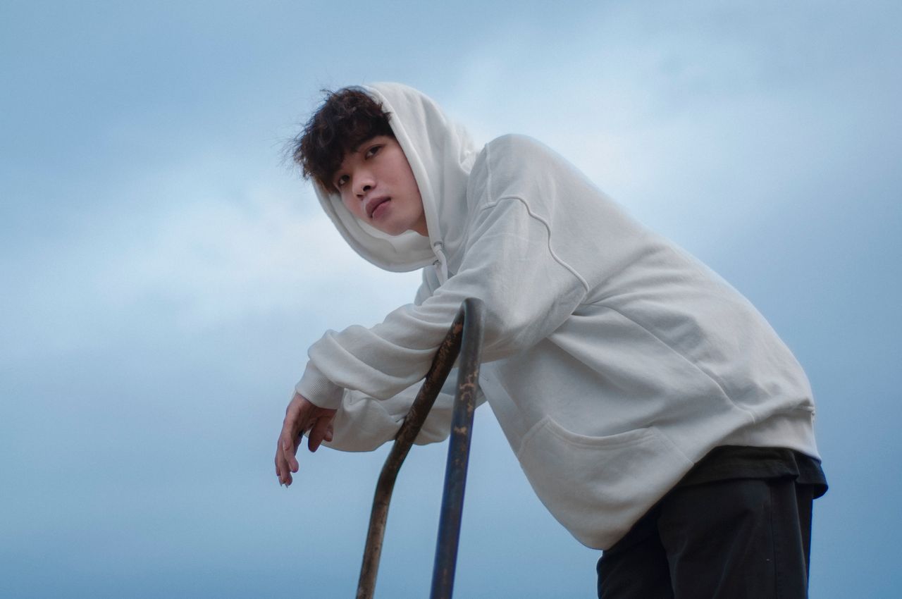 portrait of a young man in a white hoodie leaning on a metal railing u